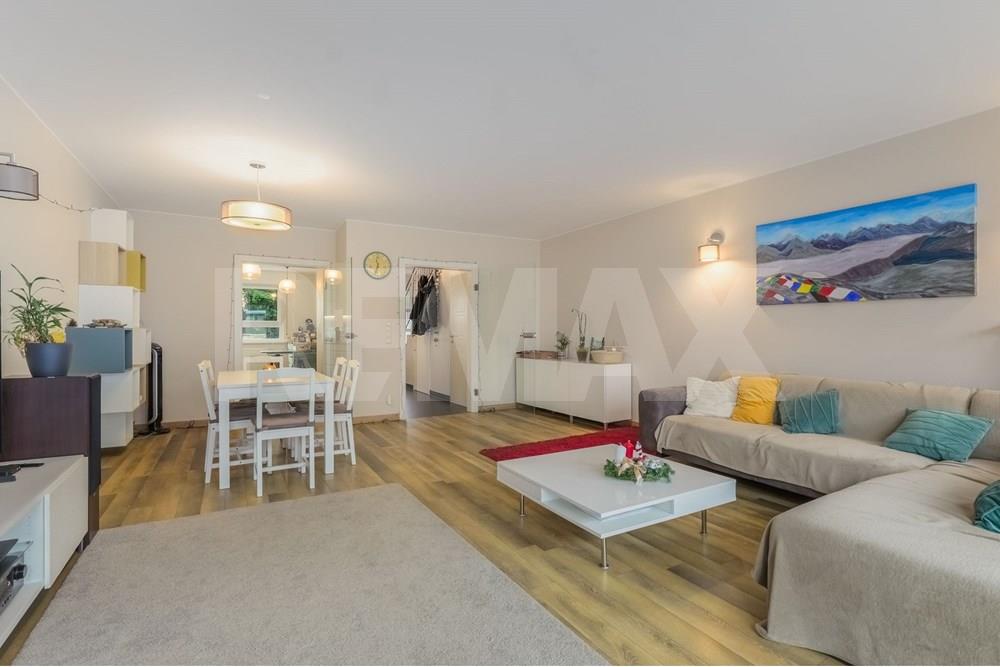 Open-plan living and dining room with sofa, white coffee table, television, dining table, and large rear windows.