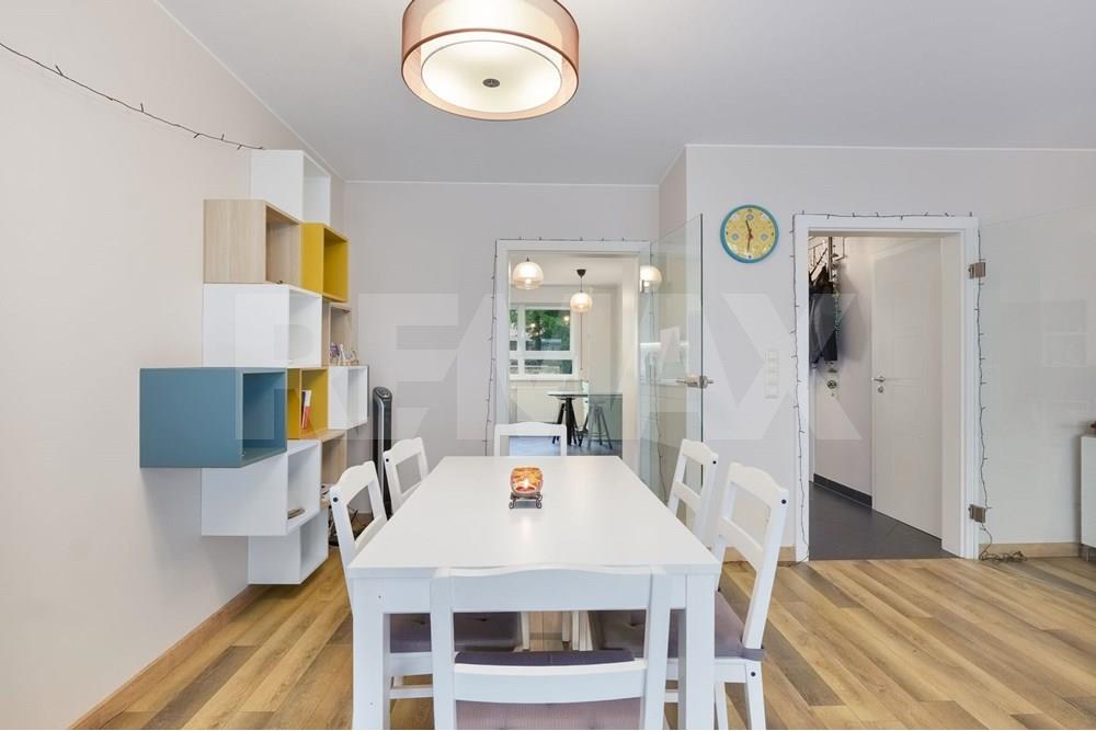 Galley kitchen with pale green fitted cabinets, integrated appliances, dark worktops, a window, and a small breakfast table.