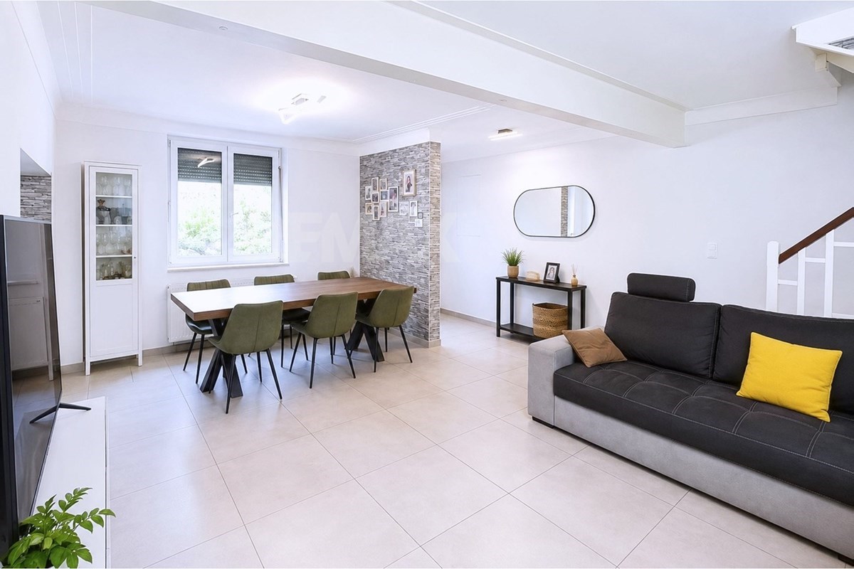 Open-plan dining area with a wood table, green chairs, a stone-pattern column, large window, display cabinet, and dark sofa.