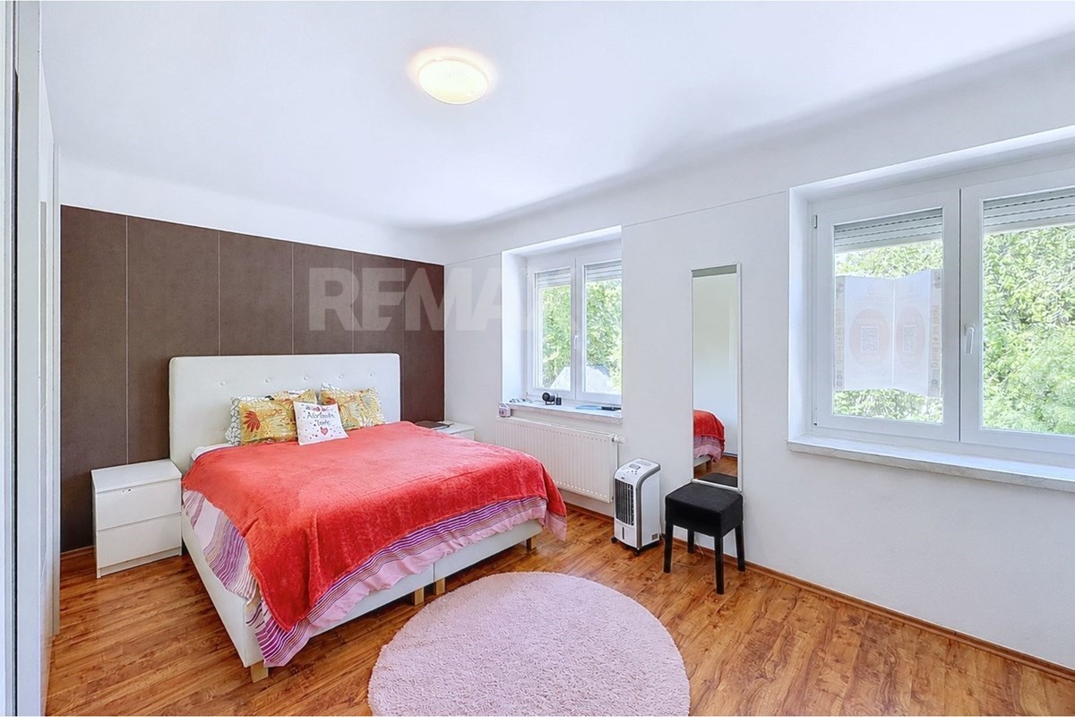 Bedroom with a double bed, coral bedding, two windows, wood flooring, full-height mirror, stool, radiator, and portable heater.
