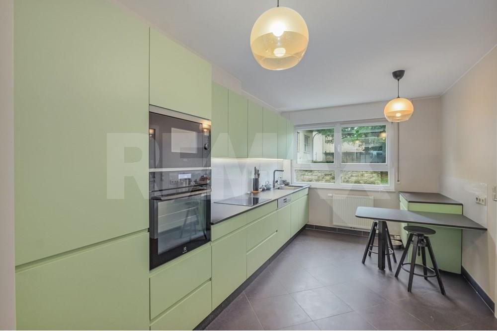 View along the fitted kitchen toward the dining and living areas, with integrated ovens, cooktop, and pale green cabinetry.