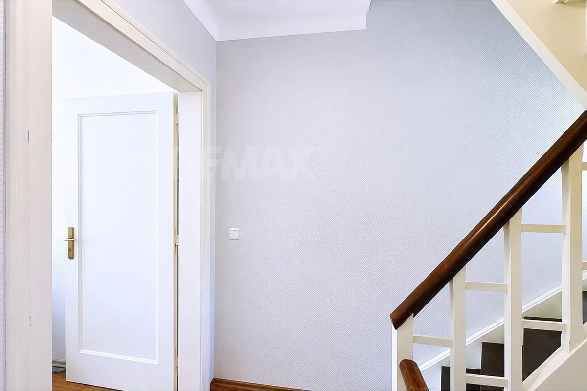 Bright landing with textured pale walls, an open white door, a wood handrail, white balusters, and visible lower stair flights.