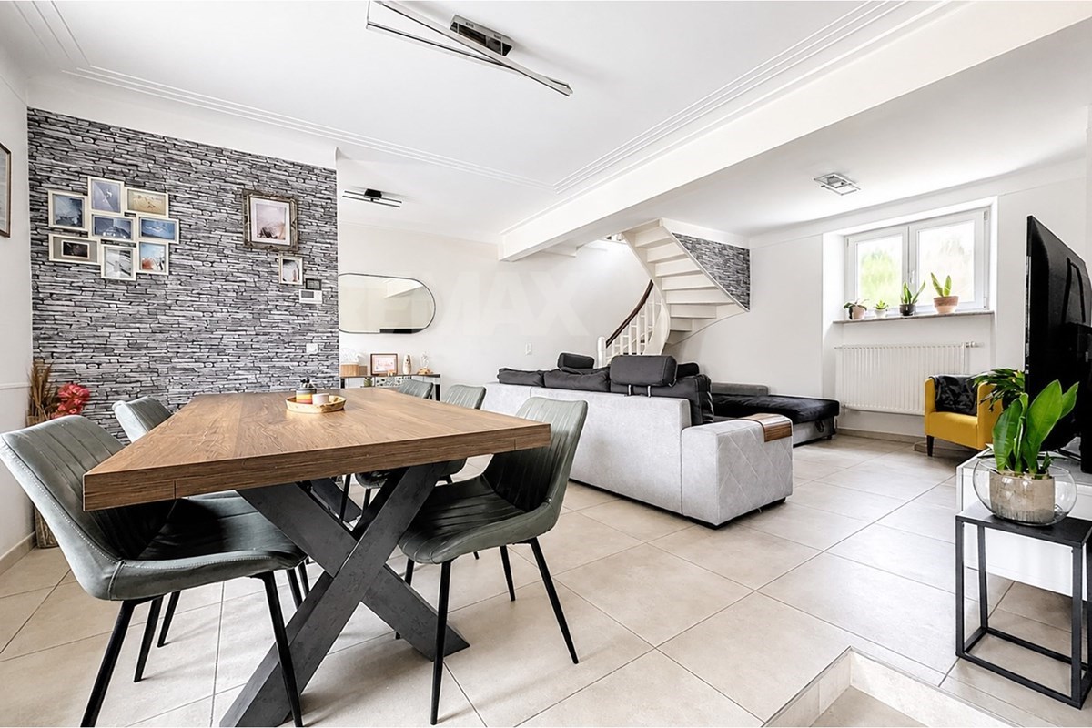Open living and dining space with a stone-pattern feature wall, dark sofa, yellow armchair, dining table, curved staircase, and large window.