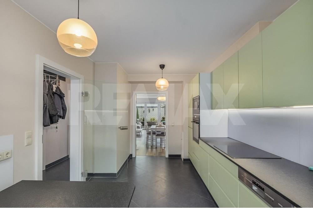 Kitchen with pale green cabinets, integrated ovens, black worktops, breakfast seating, and a window facing the outdoor area.