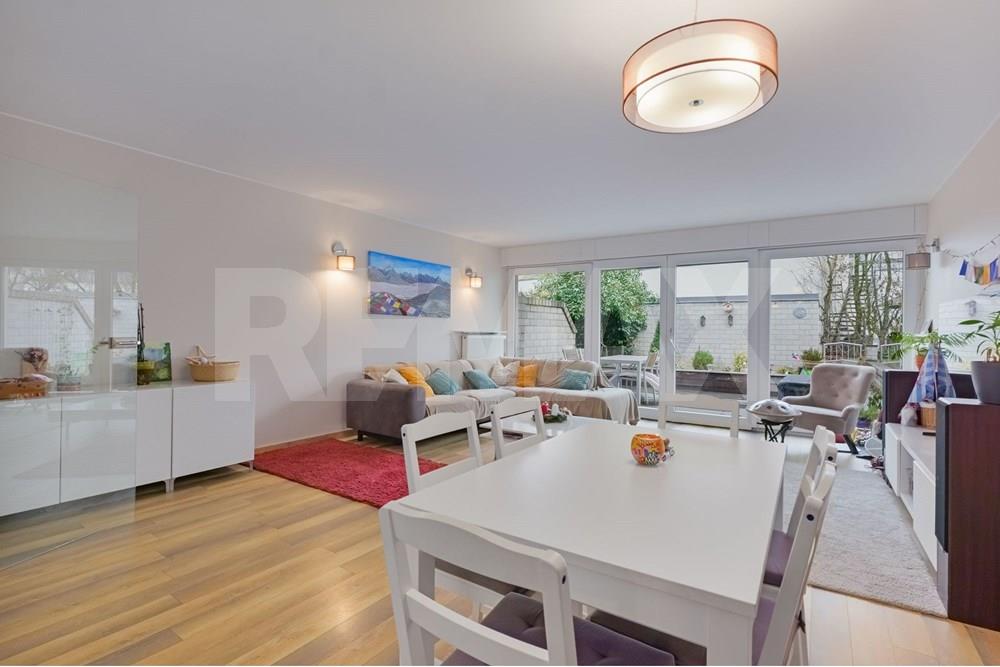 Alternate view of the bright living and dining room, showing sofas, dining furniture, shelving, and garden-facing glazing.