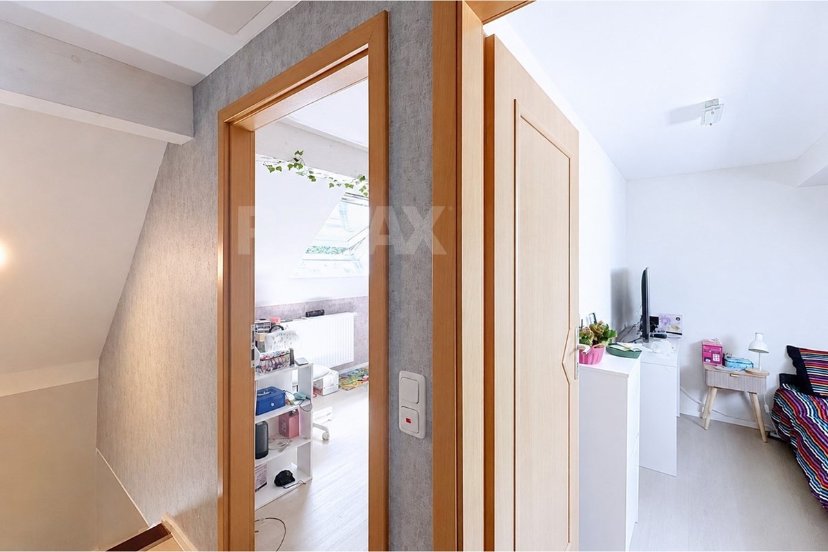 Compact upstairs room beside a large built-in wardrobe, with a TV, white desk, striped seating, and open doorway to a storage area.