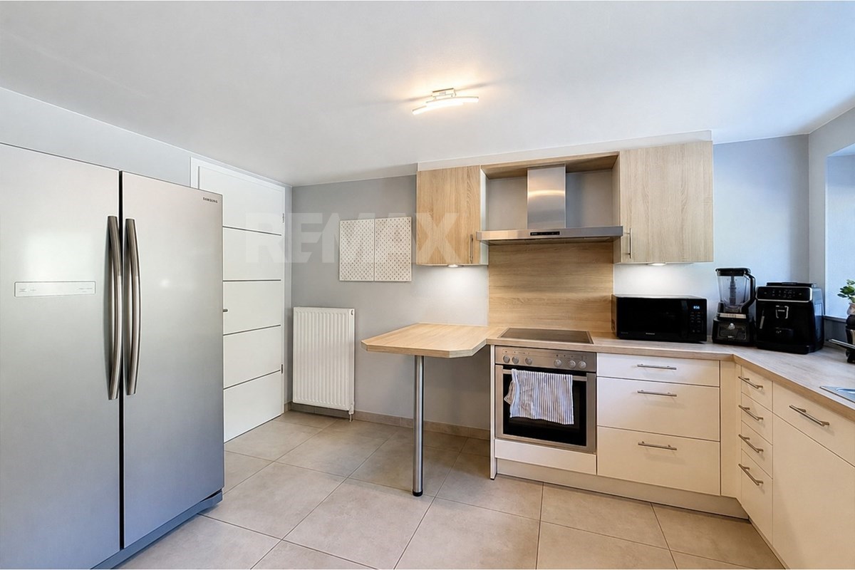 Fitted kitchen with pale wood cabinets, integrated appliances, a side refrigerator, breakfast worktop, microwave, and small appliances.